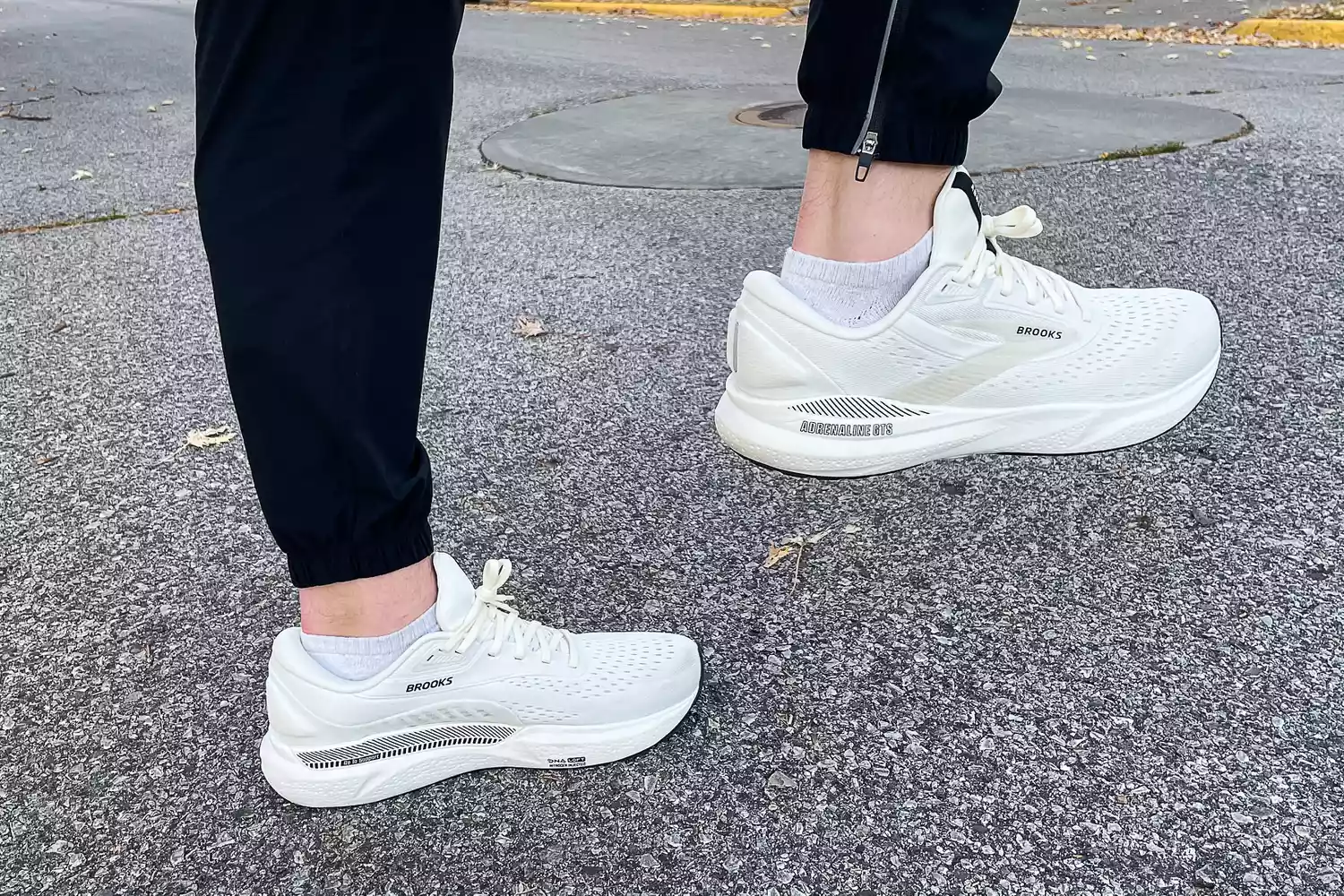 A person standing on asphalt wearing the white Brooks Adrenaline GTS 24 stability shoes.