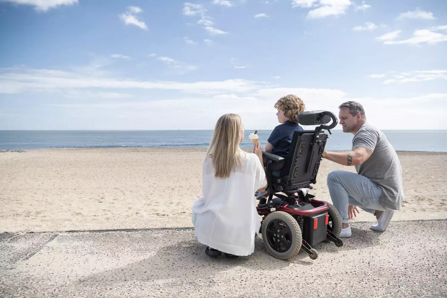 Parents with a child in a wheelchair on a beach, illustrating family wellness and health outcomes.