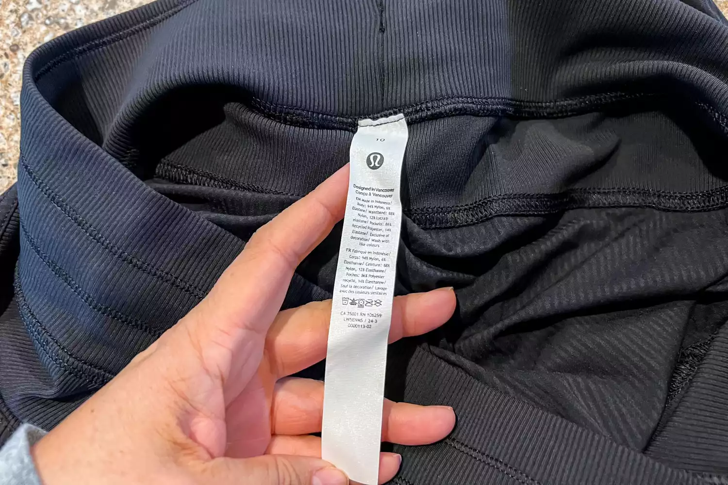 A close-up of a hand holding the care and composition tag of lululemon joggers.