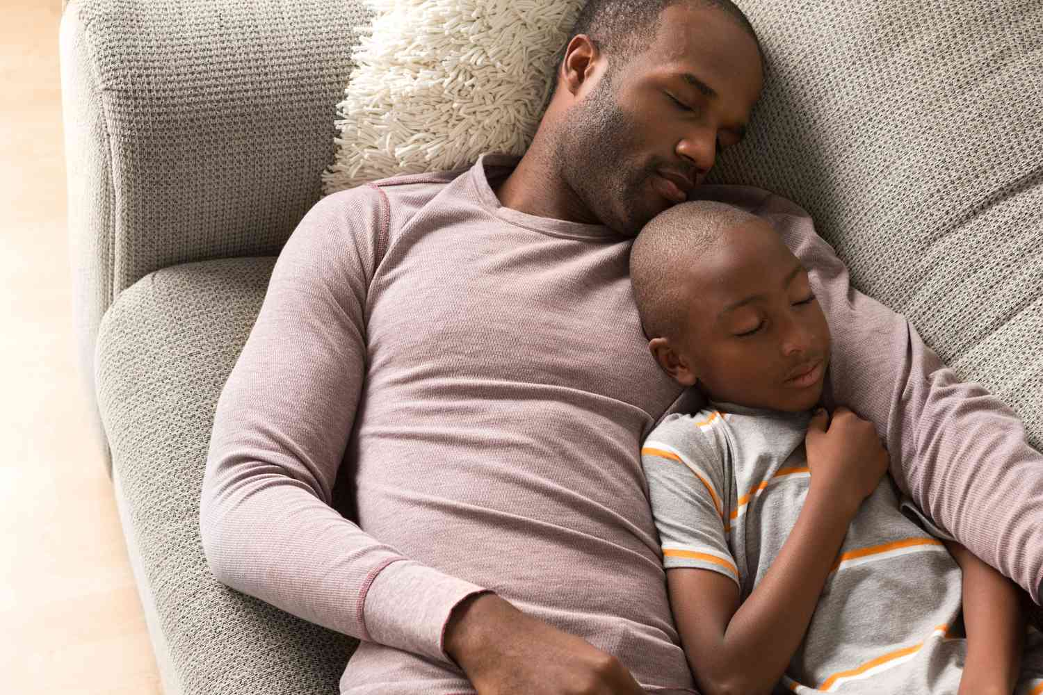 A father and son resting on a sofa, depicting physical fatigue and the need for recovery.