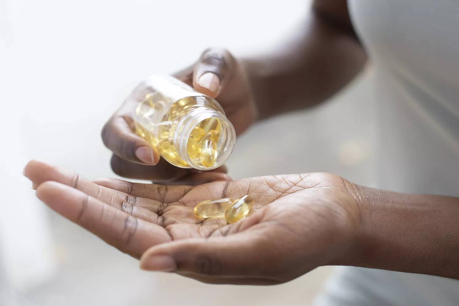 A person pouring dietary softgel vitamins from a bottle into their hand.