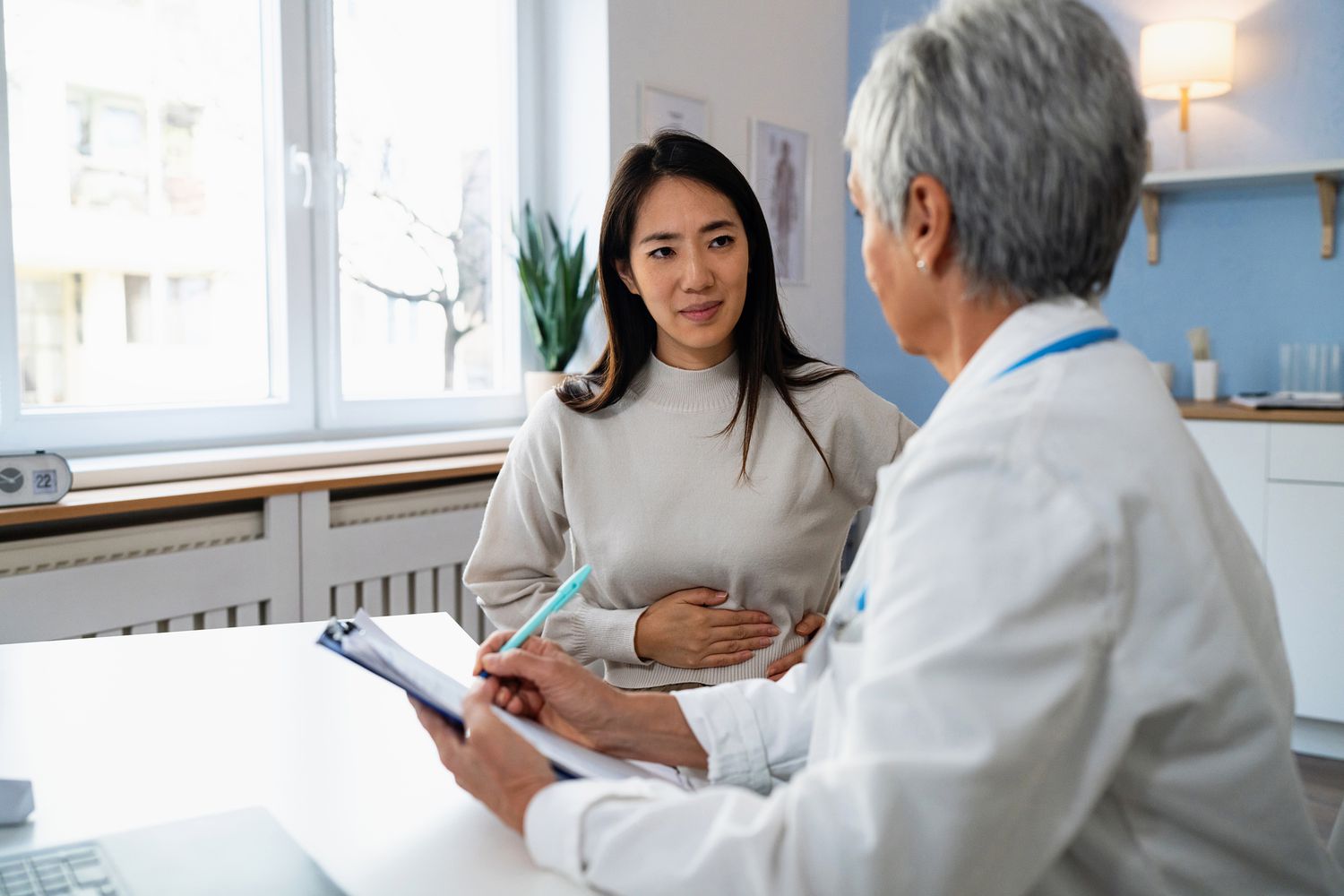 A patient holding her abdomen while describing symptoms to a healthcare provider.