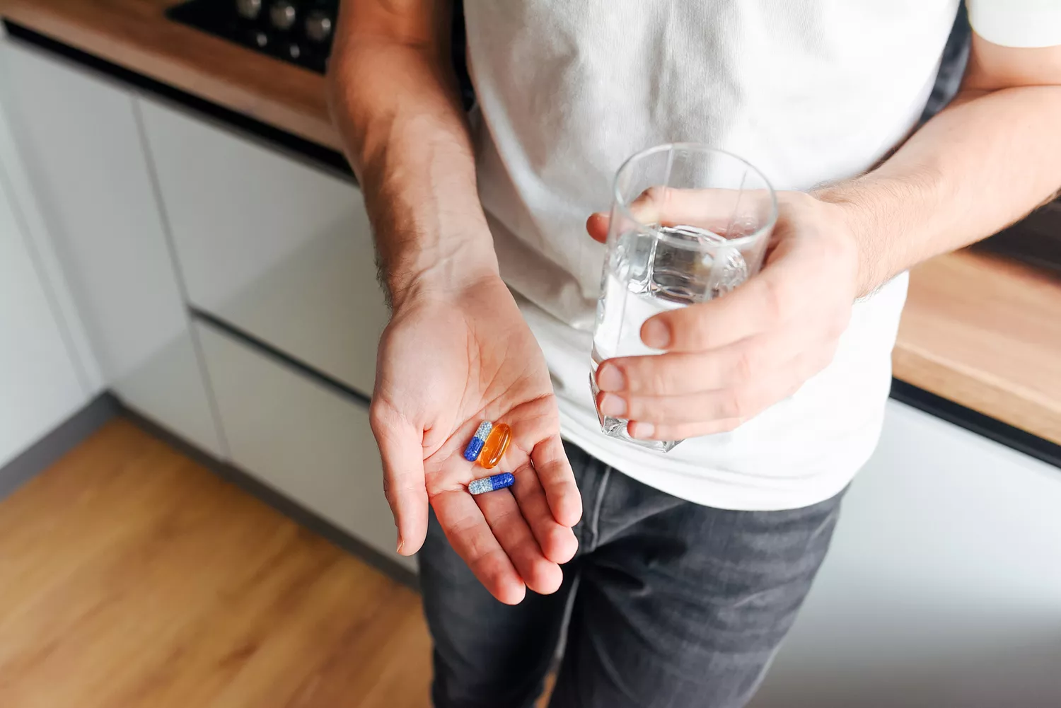 A man in a kitchen holding a handful of supplement capsules, illustrating the daily intake of health boosters.