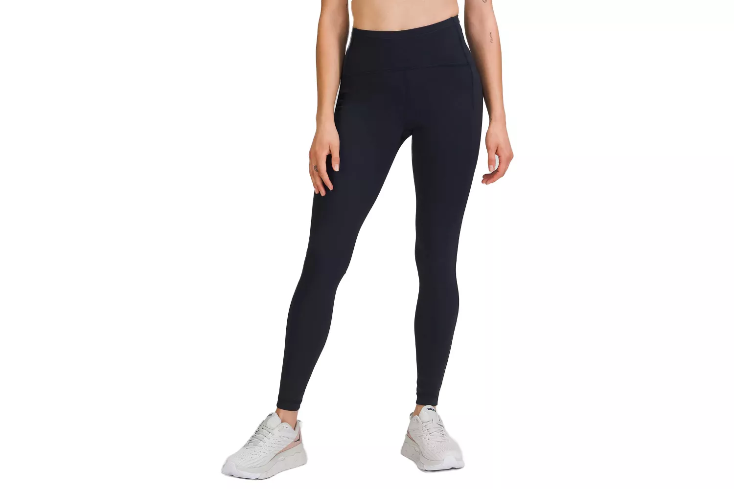 A model wearing black high-rise athletic leggings with white running shoes against a white background.