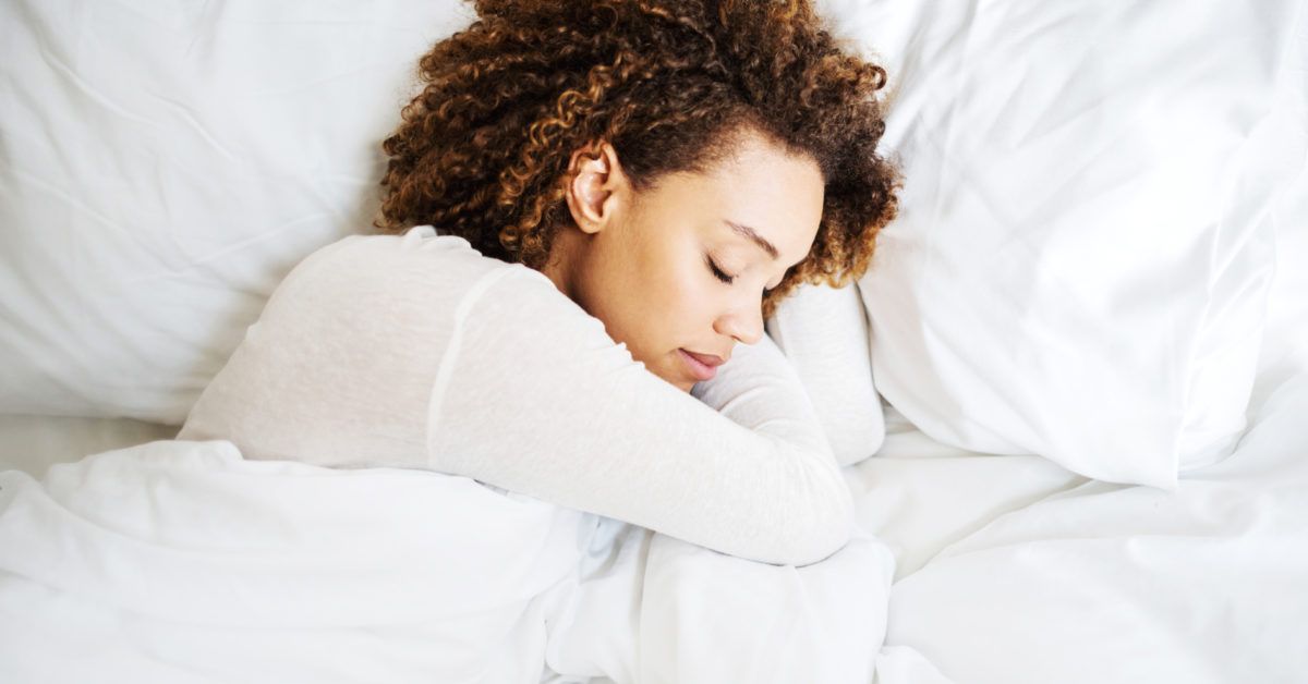 A peaceful woman with curly hair resting deeply in a comfortable bed.