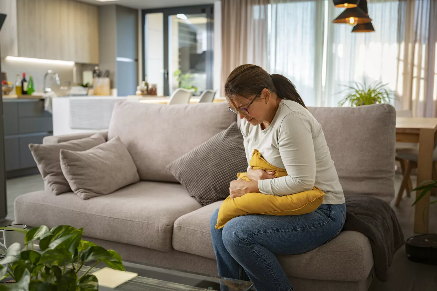 A person sitting on a couch holding their stomach, appearing to be in discomfort.