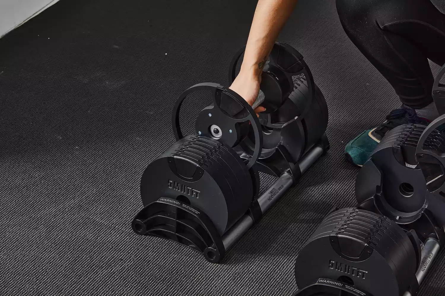 Close-up of a person hands adjusting the weight plates on an adjustable dumbbell.