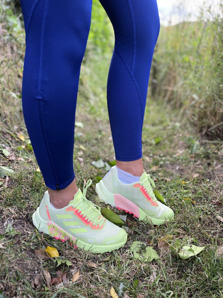 A runner equipped with a hydration vest and deep-lug trail shoes standing on a ridge.