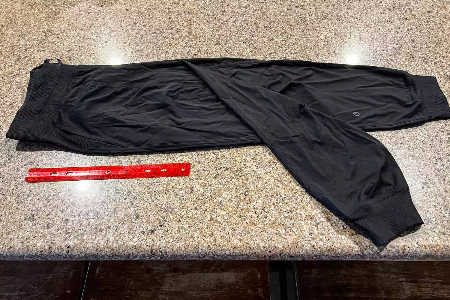 Black Lululemon joggers laid flat next to a red ruler for size comparison and technical review.
