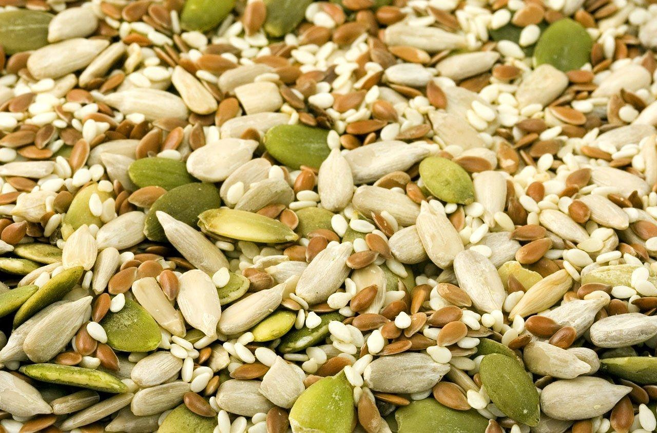 A top-down view of various bowls containing different nuts, seeds, legumes, and colorful vegetables.