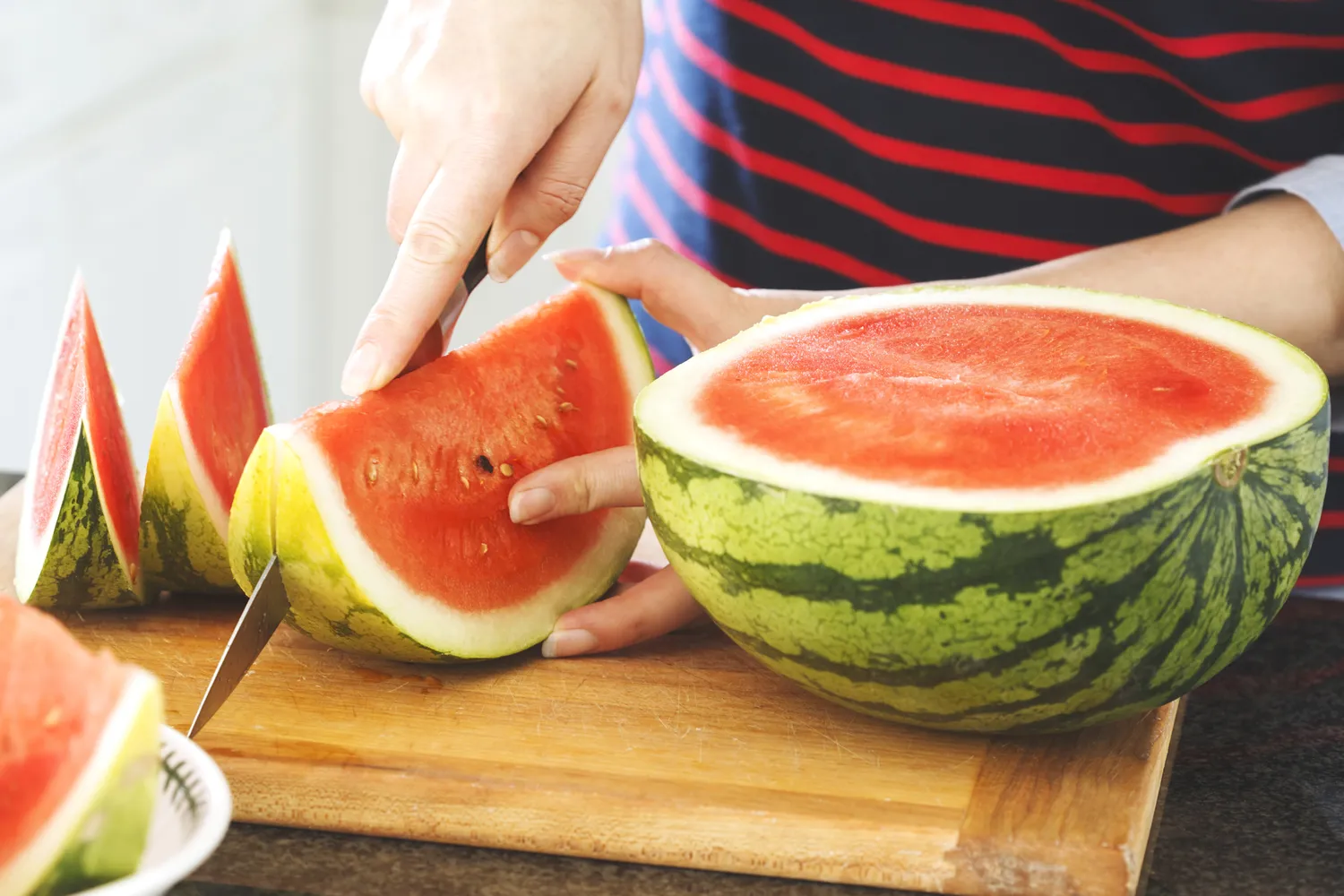 A person slicing a fresh watermelon on a clean surface.