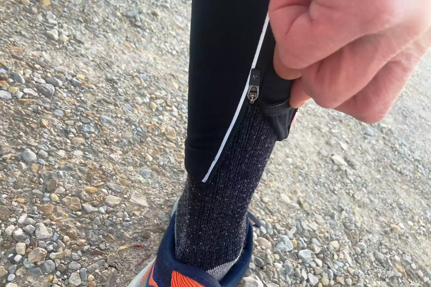 Close-up of an ankle zipper on black athletic leggings being adjusted over a running sock.