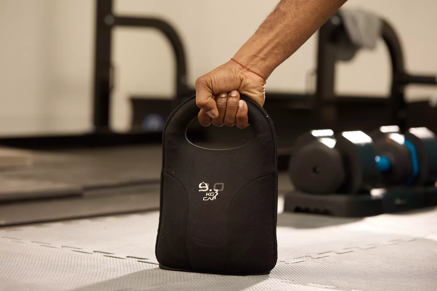 A hand holding a black 9kg CAP soft kettlebell on a protective gym mat.