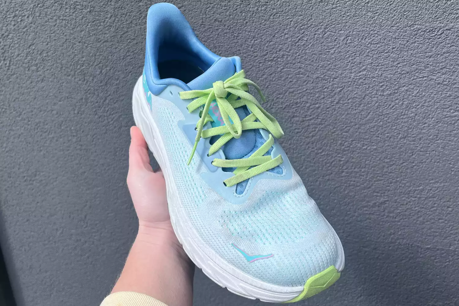 A hand holding a light blue Hoka Arahi 7 running shoe against a neutral background.