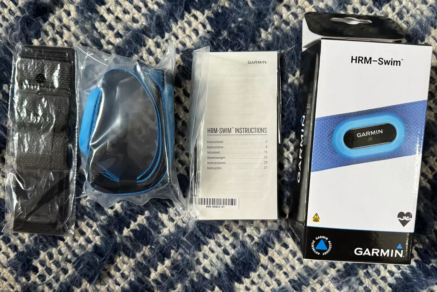 The Garmin HRM-Swim heart rate monitor unboxed, showing the sensor, manual, and the blue non-slip strap.