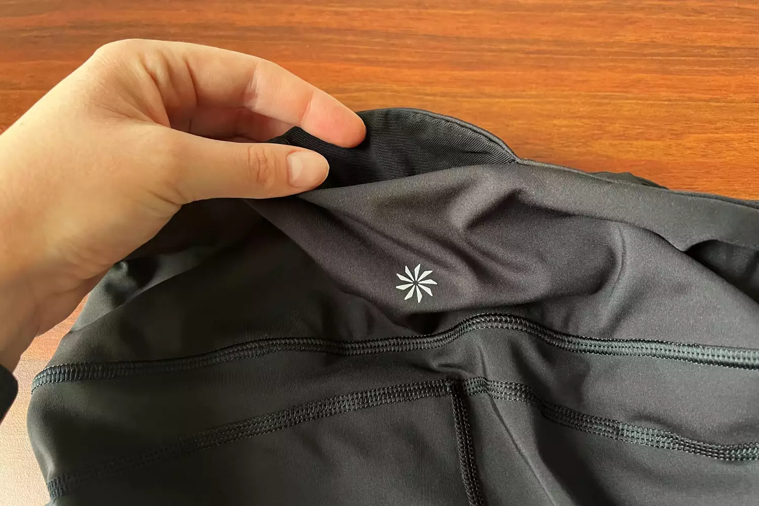 Hand lifting the waistband of dark gray athletic leggings to show the fabric detail and logo.