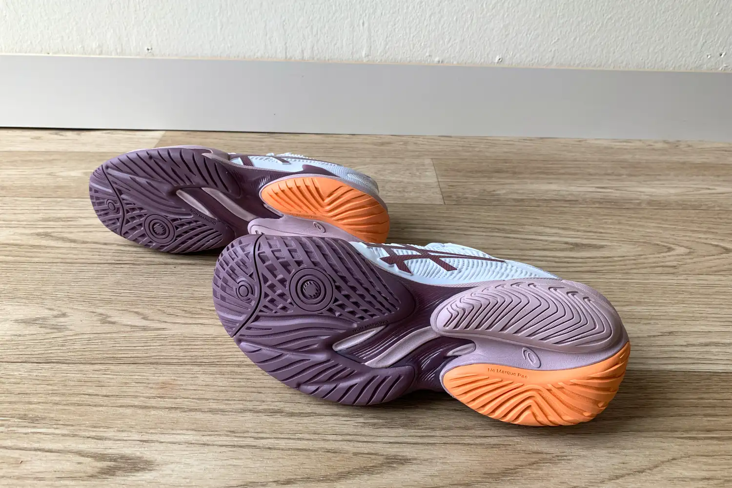 The bottom soles of Asics tennis shoes showing the purple and orange non-marking rubber tread pattern.