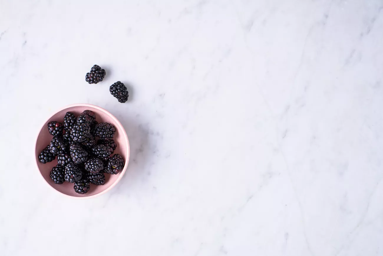 Fresh blackberries in a pink bowl on a marble surface.