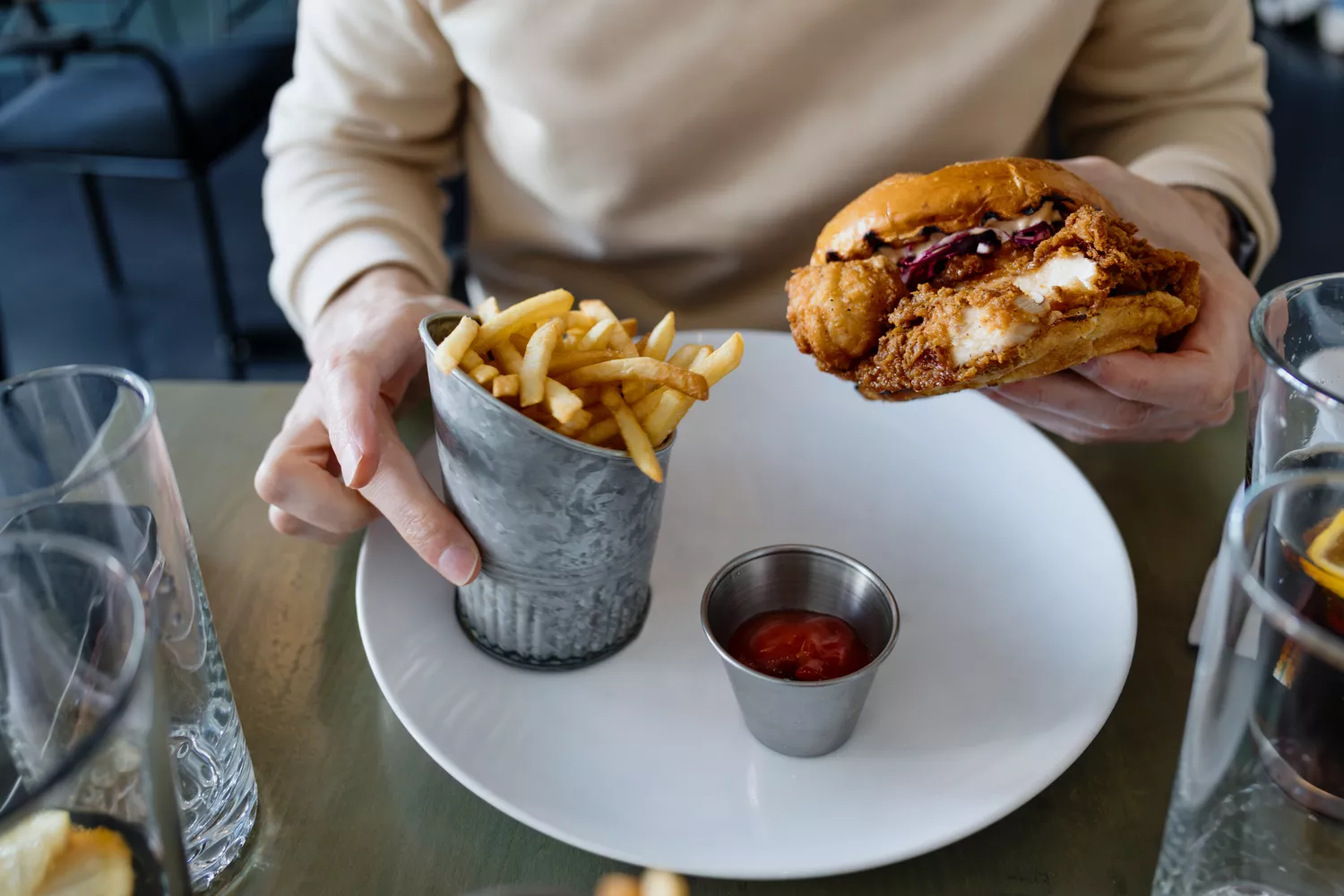 A person holding a fried chicken sandwich with a side of french fries.