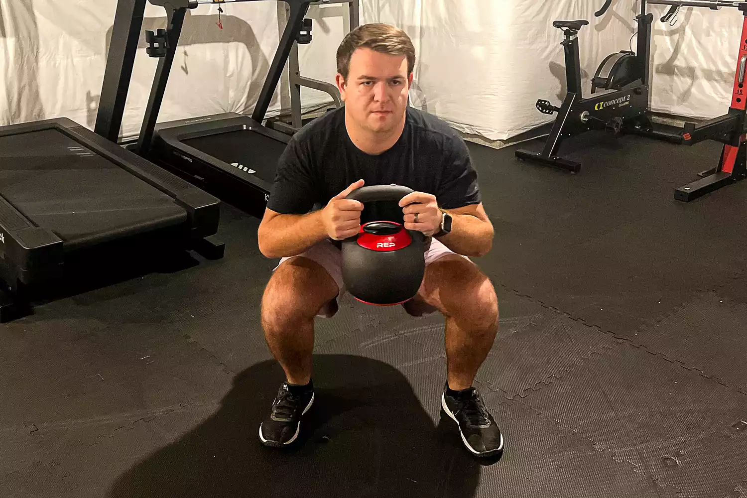 A man performing a controlled goblet squat with a REP Fitness adjustable kettlebell.