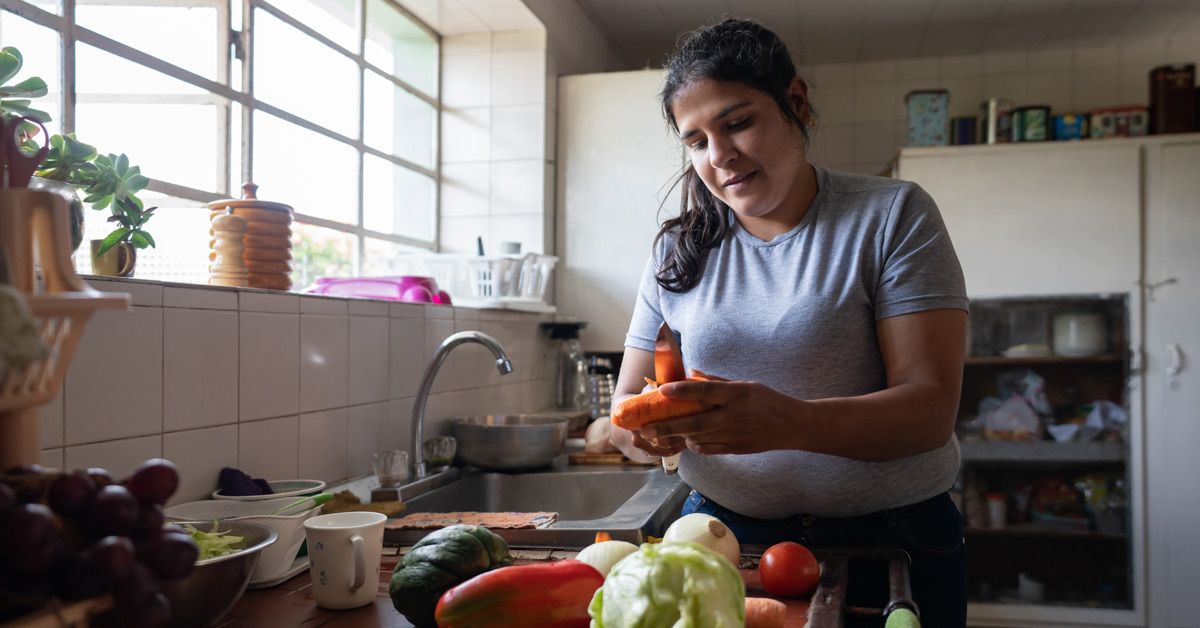 A woman in a kitchen preparing fresh vegetables such as carrots for a healthy meal.