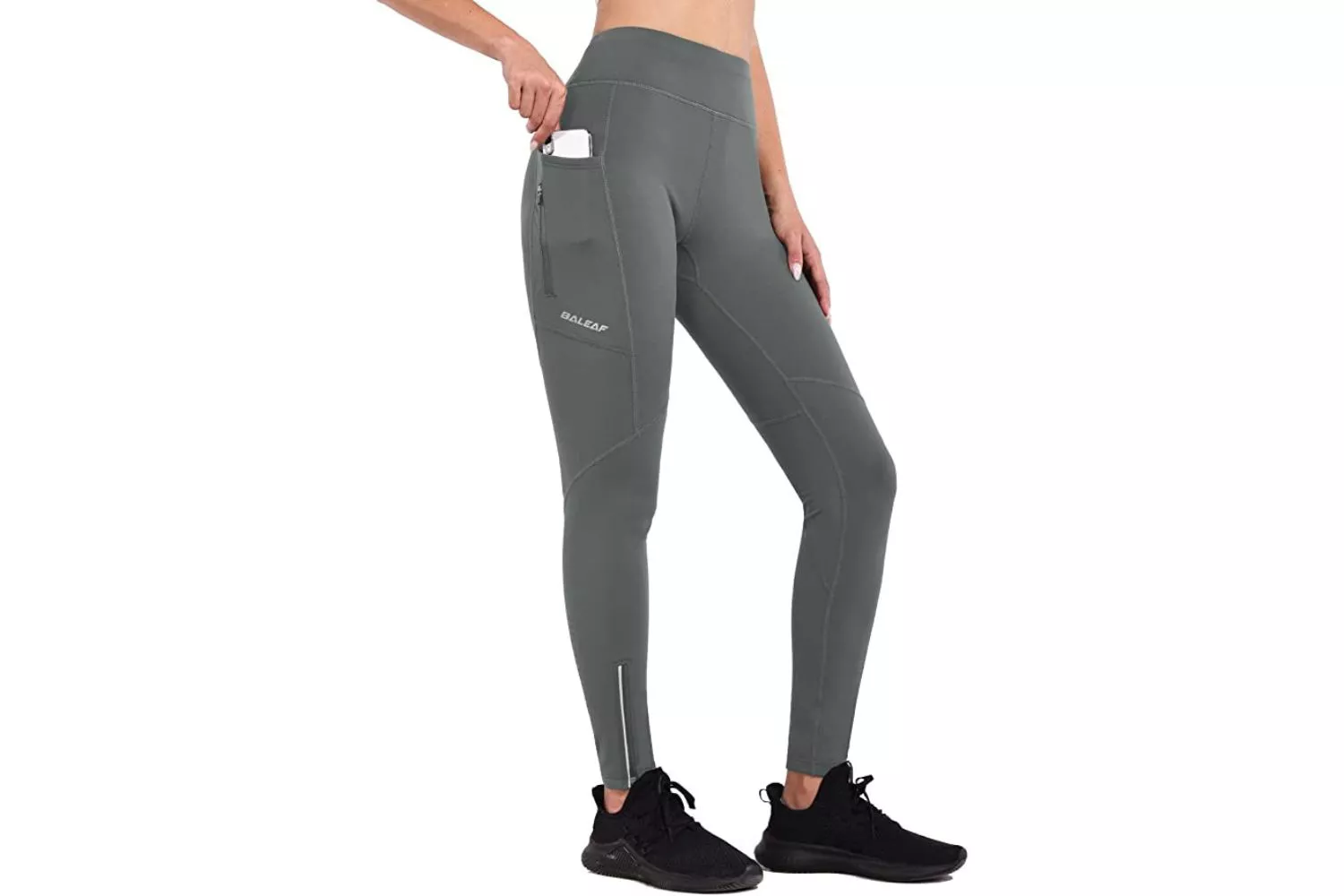 A woman inserting a smartphone into the side pocket of her black athletic leggings.