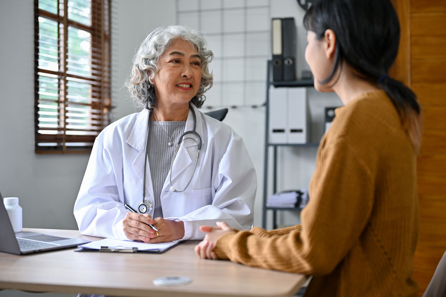 A healthcare provider taking notes while consulting with a patient in a professional medical office.