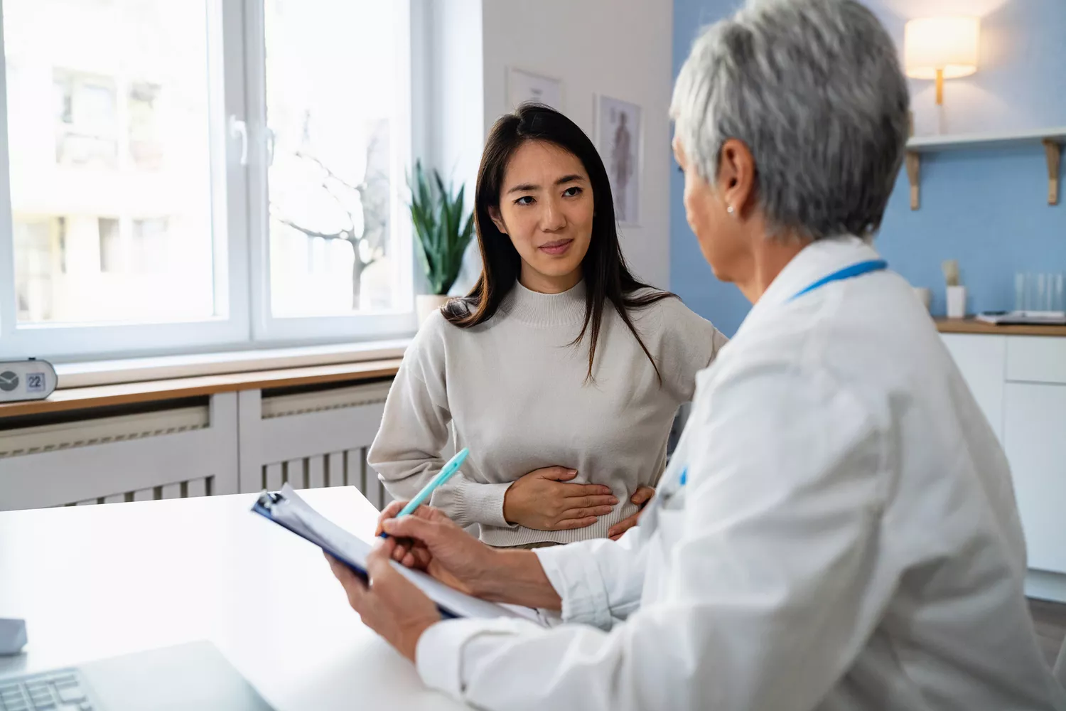 A doctor taking notes during a clinical discussion with a female patient regarding her symptoms and health history.