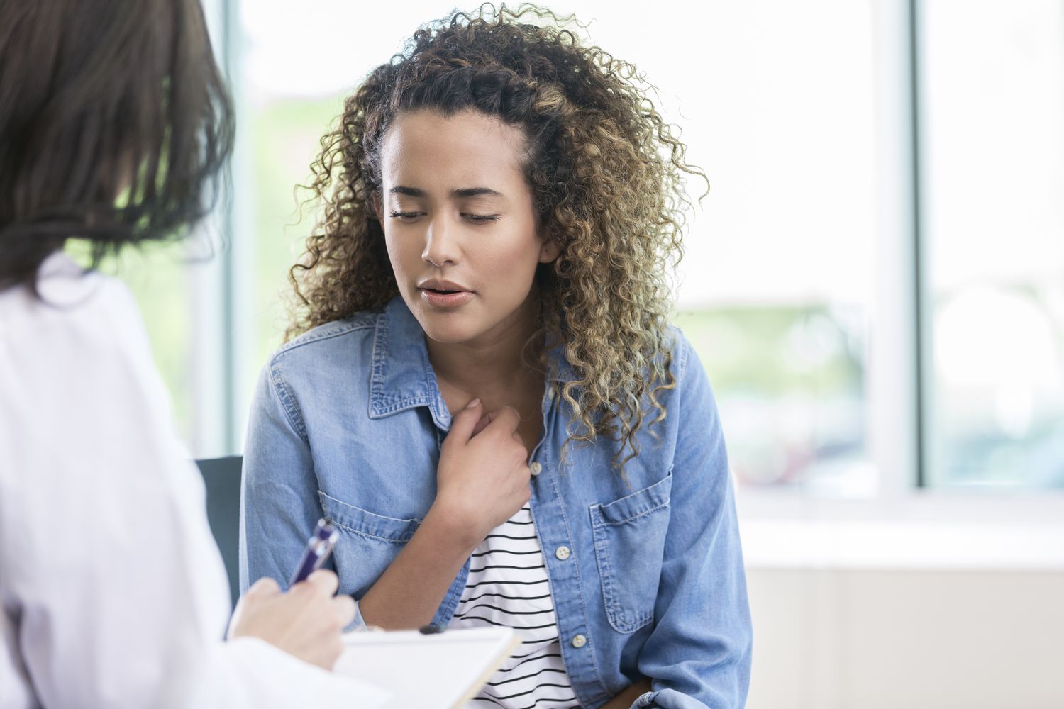 A woman holding her chest while speaking with a healthcare professional in a clinic.