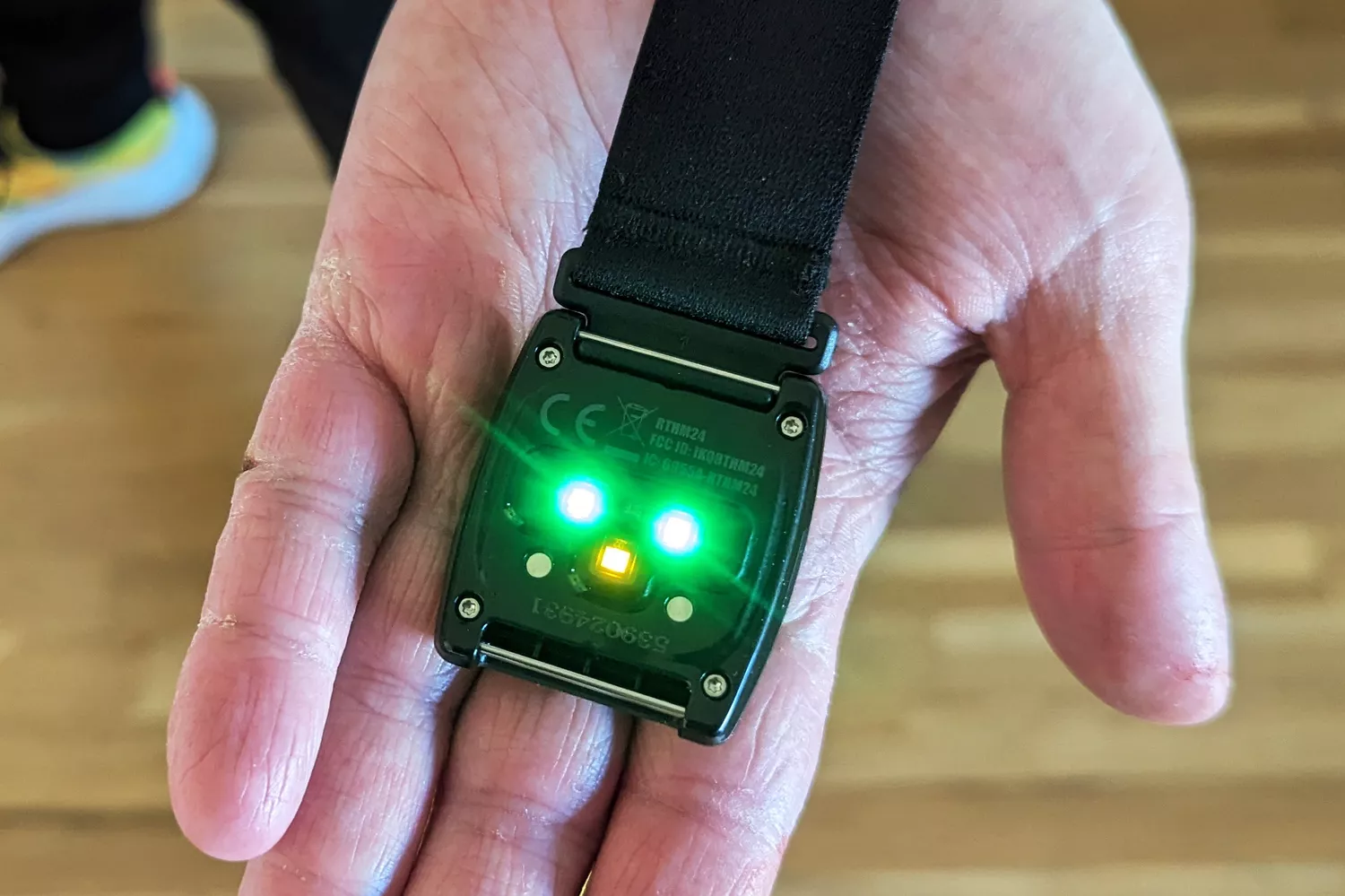 A close-up of a heart rate monitor armband showing the glowing green optical sensors on the underside.