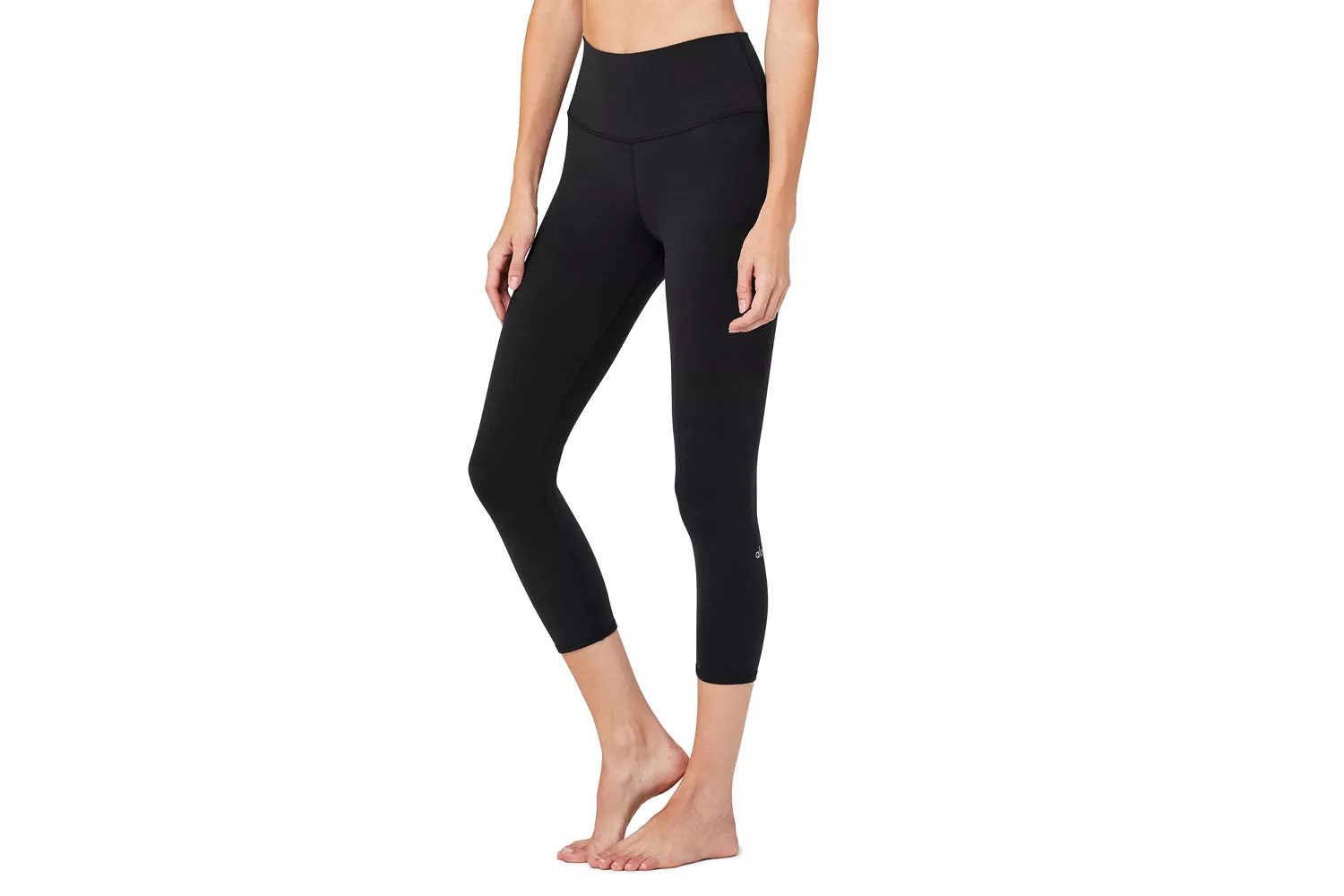 A woman models black high-waist capri-length leggings against a white background.