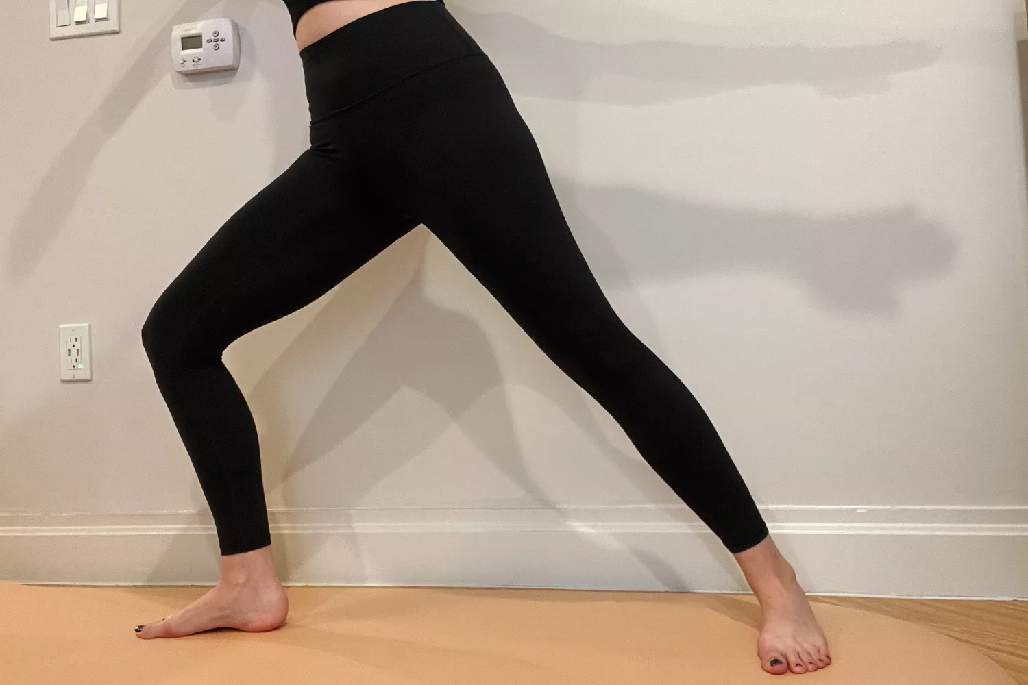 A person performing a warrior II yoga pose on a mat, wearing black Athleta leggings.