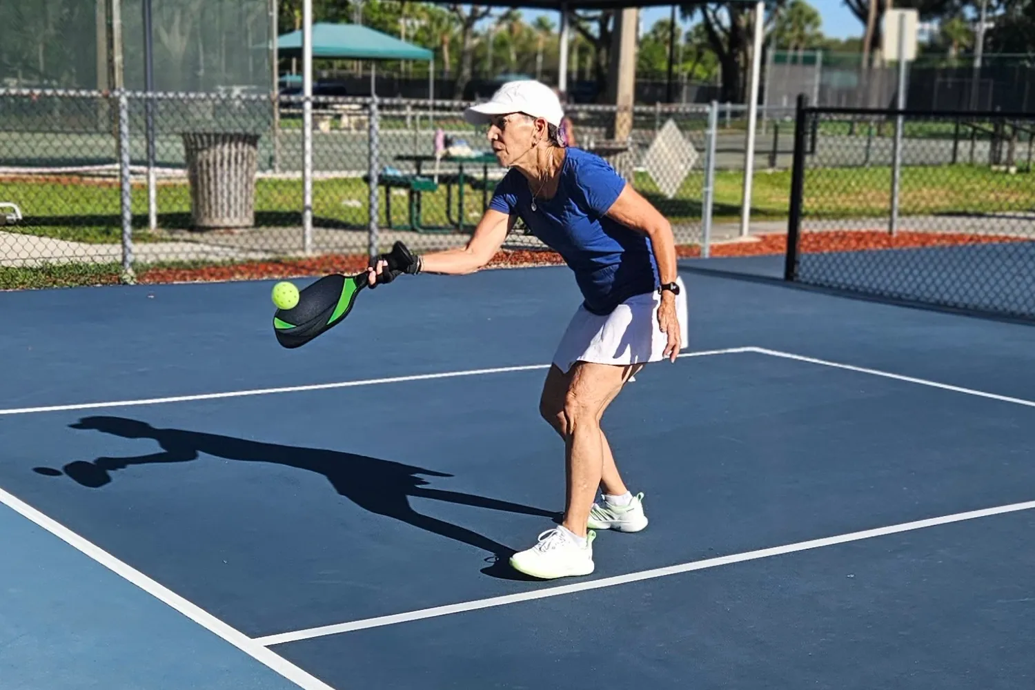 An older woman playing pickleball outdoors under bright Florida sunlight.