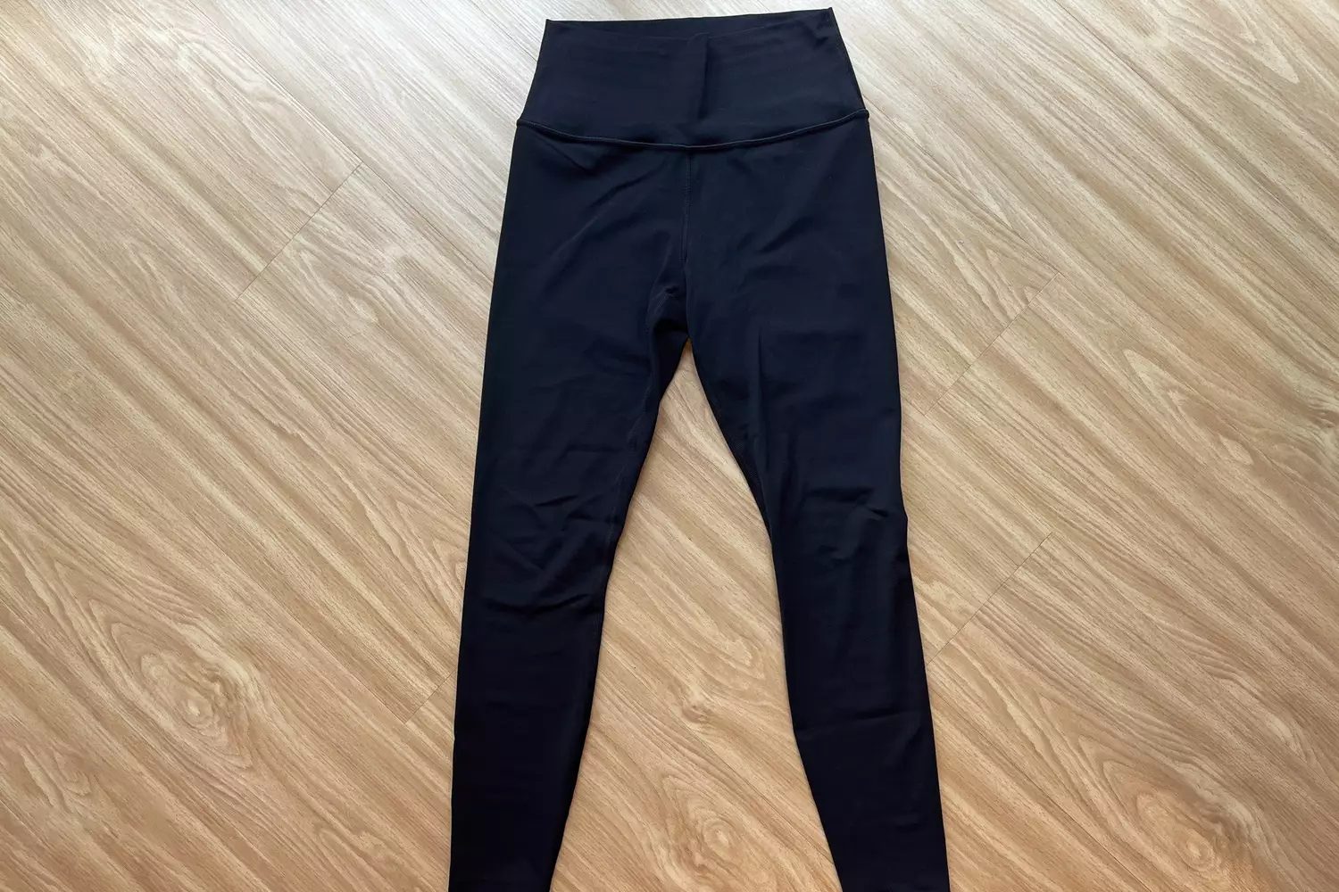 Black high-waisted Athleta leggings laid flat on a light wood floor.