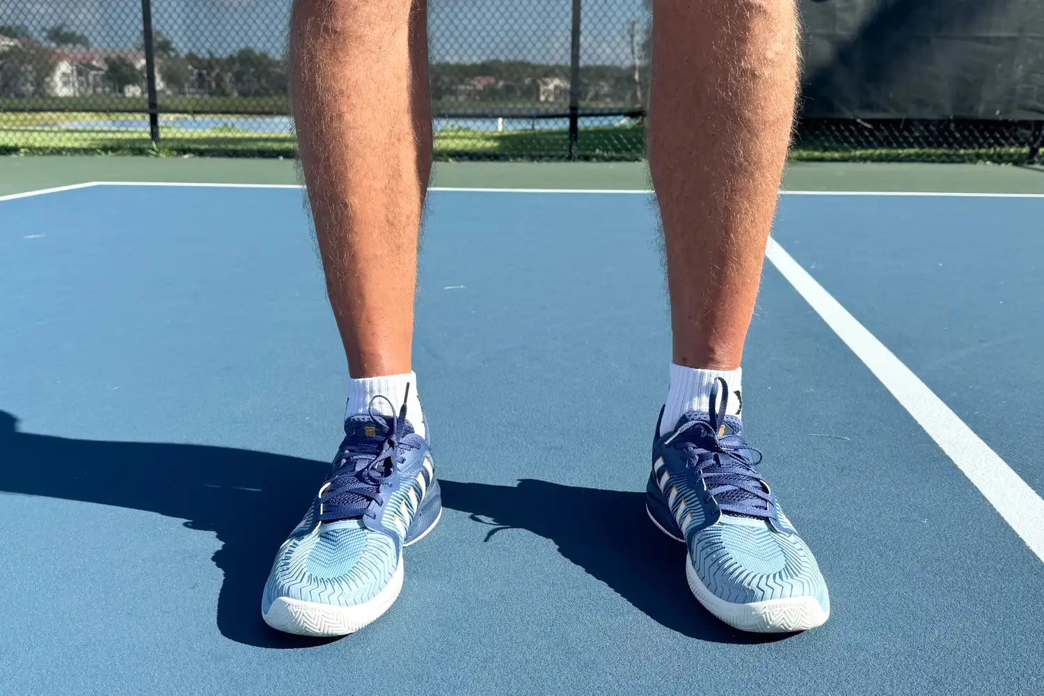 Close-up of a player's legs and athletic shoes in a ready stance on a court surface.