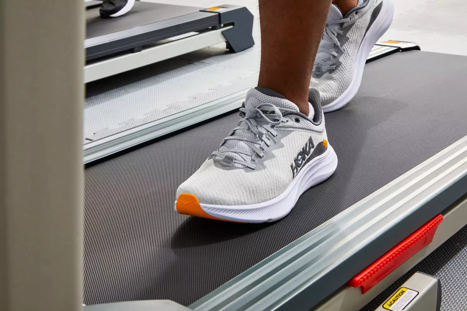 A person wearing Hoka shoes while running on a treadmill in a gym.