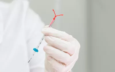 A healthcare provider in blue gloves holding an IUD and its insertion delivery system.