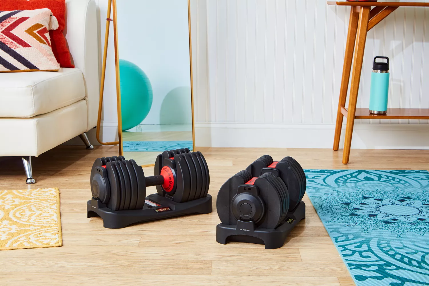 Two adjustable dumbbells on compact stands positioned in a modern living room next to a fitness ball.