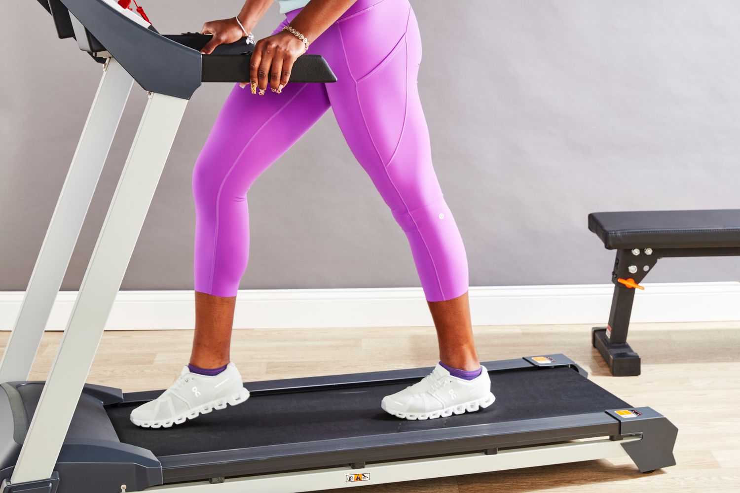 A woman in purple leggings and sneakers walking on a treadmill indoors.