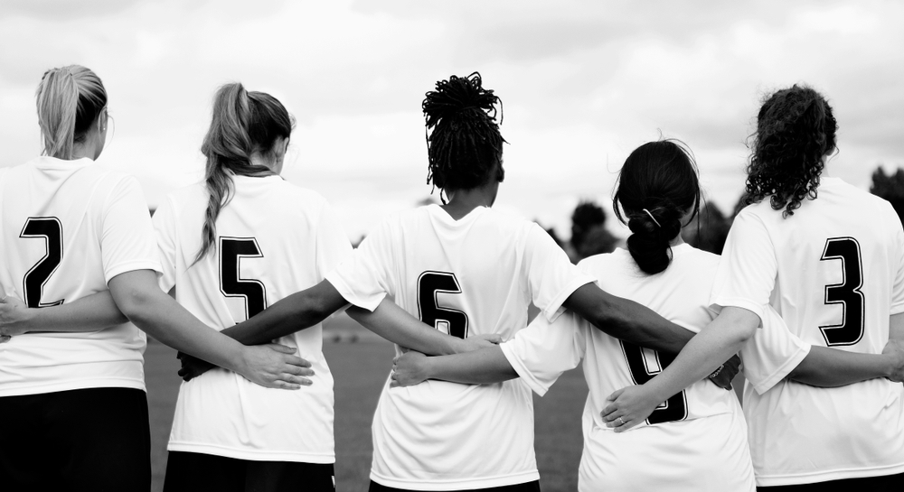 Female athletes in a huddle on a football field during a training session.