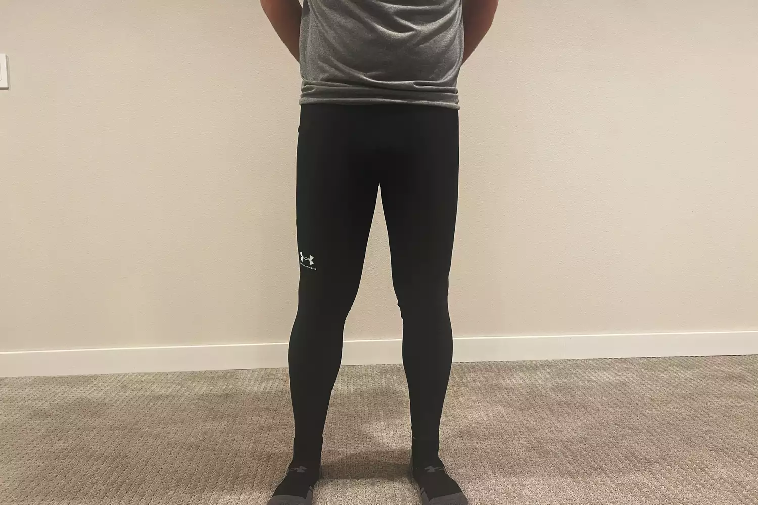 A person standing in a home gym setting wearing Under Armour leggings and a t-shirt.