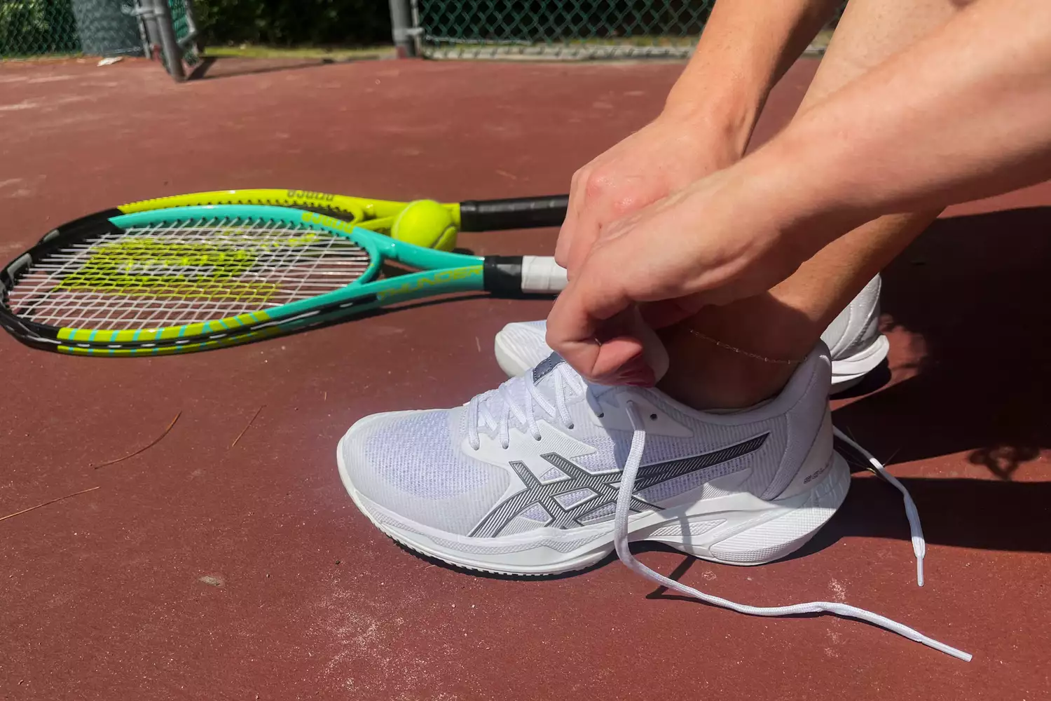 A person tying the laces of a white tennis shoe on a court, focusing on a secure fit.