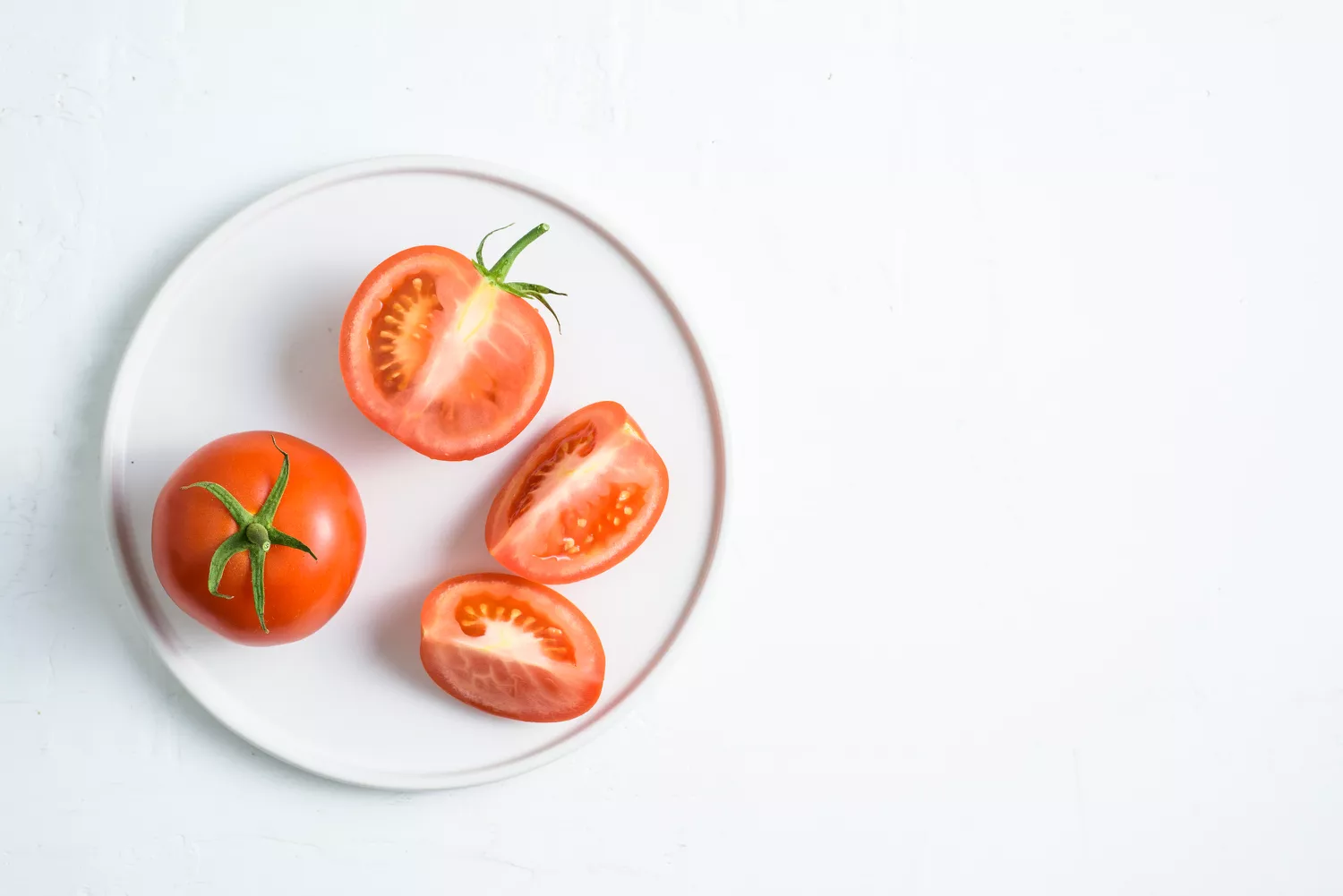 Whole and sliced fresh red tomatoes on a white plate.