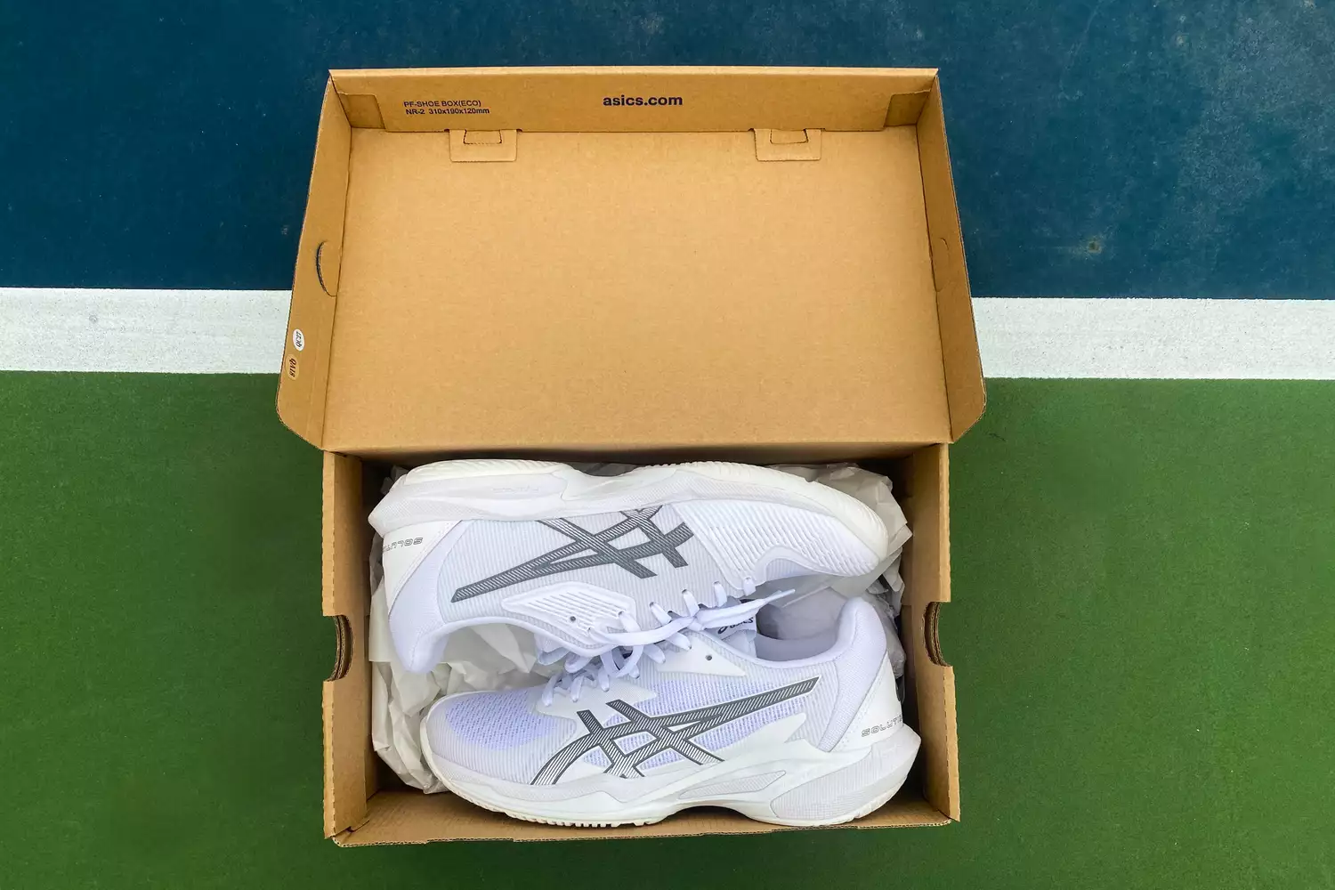 A new pair of white Asics Solution Speed FF 3 shoes in their box on a blue and green court.