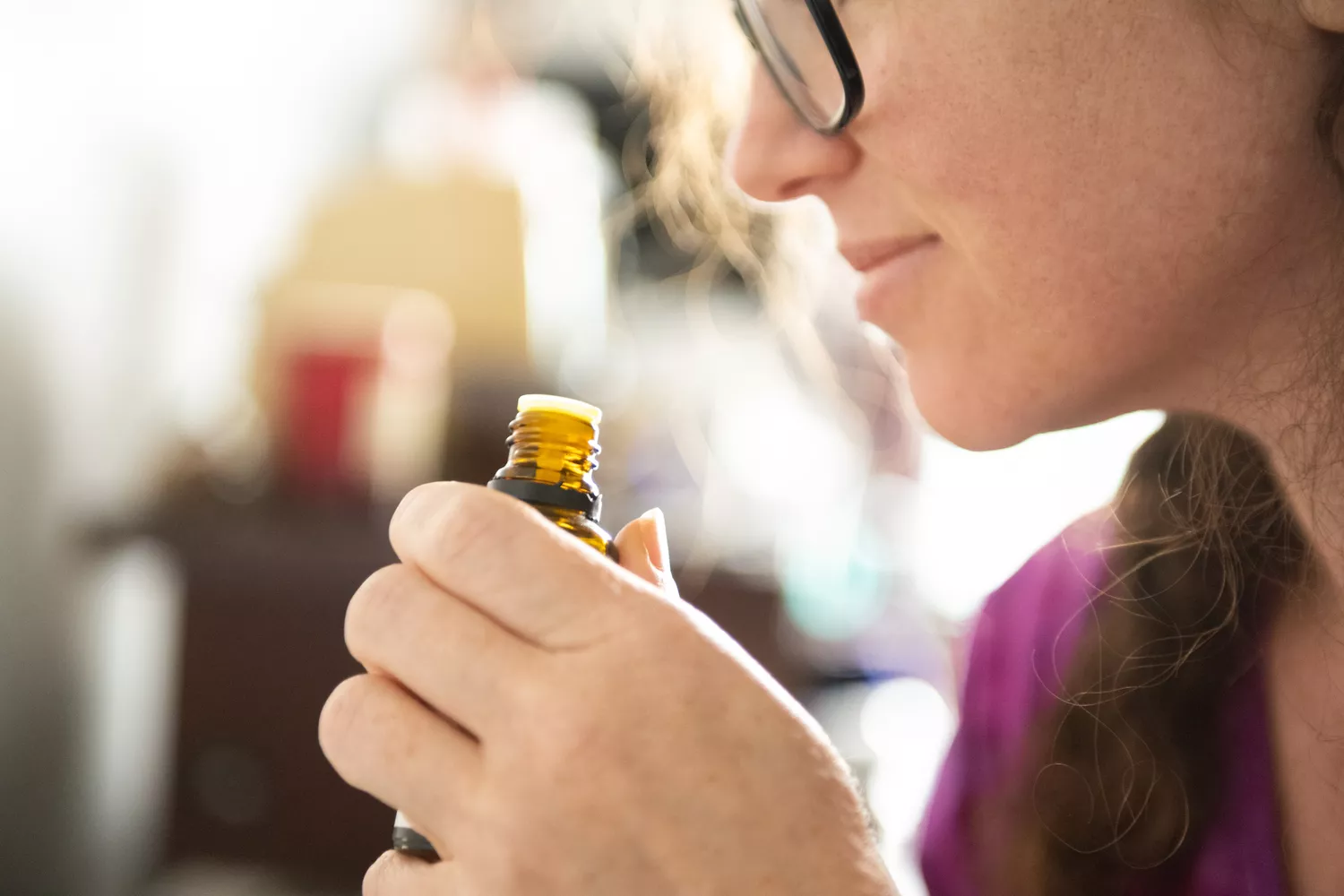 A woman closing her eyes and smelling a small bottle of oil, representing a holistic wellness routine.